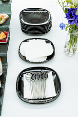 Table setting, black plates are stacked on the table, a set of teaspoons is lying on a plate,...