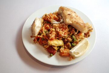 Top view, homemade paella and grilled fish on white plate and table. 