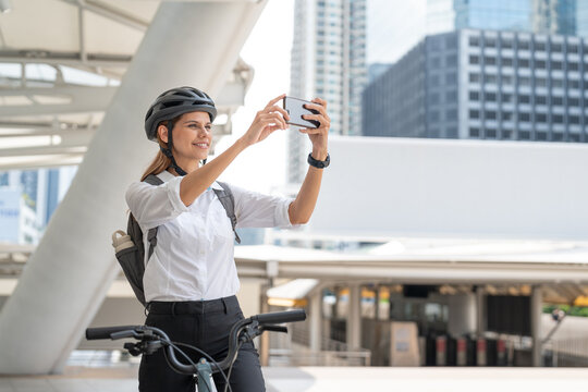 Businesswoman using smartphone take photo while riding bicycle. Woman commuting on bike go to work in city. Eco friendly vehicle, sustainable lifestyle concept