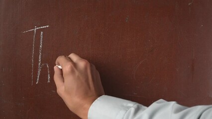 Textured brown chalkboard background. Male hand writing 'thank you' on the board with a piece of white chalk in close up.