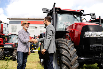 Farmer and dealer shaking hands after successful tractor purchase. Investing in farming equipment.