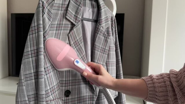 a woman smoothes a plaid jacket with a steamer, ironing clothes at home