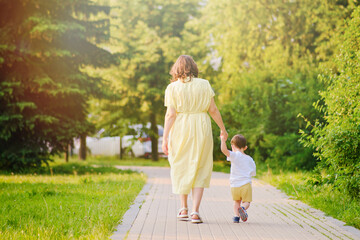 A child takes steps holding a mother woman by the hand along a path in nature. Happy baby with mom...