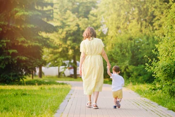 Foto op Aluminium A child takes steps holding a mother woman by the hand along a path in nature. Happy baby with mom on a walk in the summer park. Kid aged about two years (one year eleven months) © Андрей Журавлев