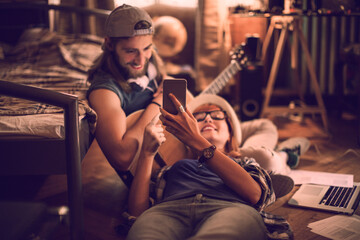 Fototapeta na wymiar Loving young couple looking at the smartphone while playing guitar in the bedroom