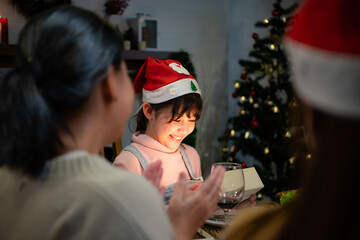 Cute little girl in Santa hat opening Christmas present and smiling.