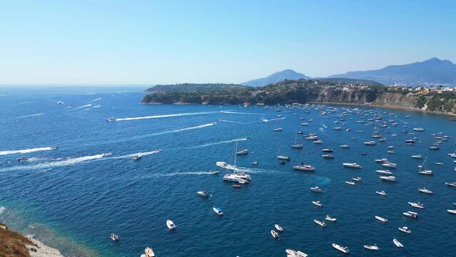 Bright aerial pan right shot from Panoramica sulla Corricella on Procida Island (Isola di Procida) encompassing the cobalt Tyrrhenian Sea in the Gulf of Naples, white boats, Vesuvius, pastel buildings