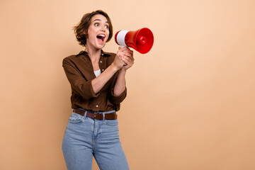 Photo of shiny excited girl dressed brown shirt screaming bullhorn empty space isolated beige color...