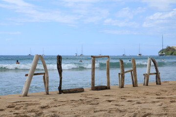 Driftwood Aloha Sign on Beach with sailboats in background
