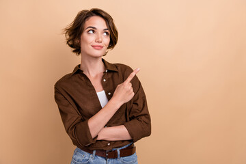 Photo of dreamy shiny girl dressed brown shirt looking showing finger empty space isolated beige color background