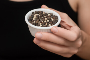 Bowl filled with natural aromatic Black and White pepper in female hand. White small bowl with...