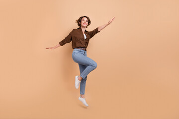 Full length photo of positive carefree girl dressed brown shirt jumping high flying empty space...