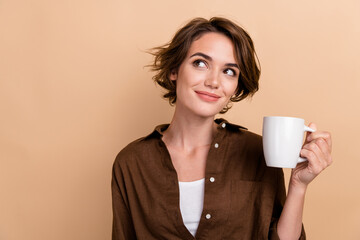 Photo of funny thoughtful girl dressed brown shirt enjoying tea looking empty space isolated beige...