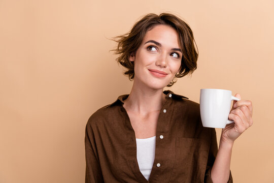 Photo of funny thoughtful girl dressed brown shirt enjoying tea looking empty space isolated beige color background