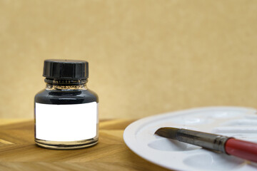 Black ink bottle with empty white label with ink brush and a palette, yellow background.