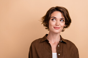 Photo of positive optimistic woman with bob hairstyle dressed brown shirt look at promotion empty space isolated on beige color background