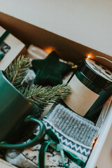 Close-up of Christmas gift box. Cozy mug for coffee, warm gray socks, aroma candle in jar. - 667750561