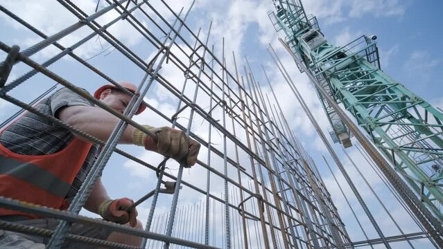 A worker uses steel tying wire to fasten steel rods to reinforcement bars. Reinforced concrete structures - knitting of a metal reinforcing cage.