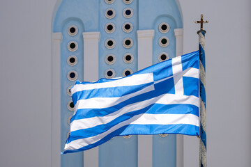 View of the greek flag waving in the air and a whitewashed church in the background in Ios Greece