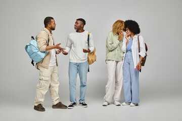 young women whispering secretly to each other next to their male friends on gray backdrop, students