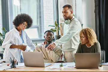 thoughtful team of friends in bold attires looking at laptop and discussing project, working process