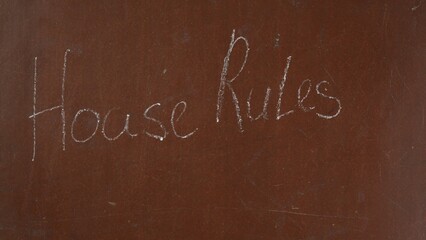 Textured brown chalkboard background. 'House rules' is written on the board with a piece of white...