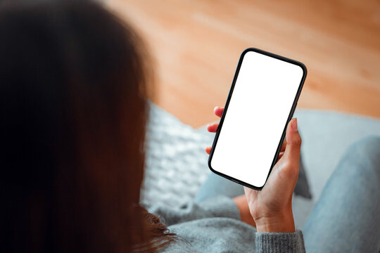 Hand of woman holding mockup blank screen mobile smartphone on sofa at home, White empty space for advertise text