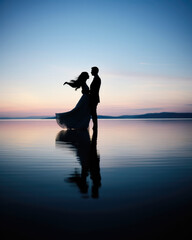 Serene Moment: Bride and Groom Embracing Love by the Lake at Sunset, minimalist landscape with blue and pink color, the bride in a princess dress and her hair blowing in the wind
