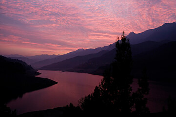 A curvy river reflecting the beautiful pink sunset sky over the mountains silhouettes. Copy space, background.