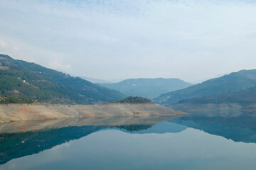 Beautiful view of mountain lake on a calm foggy day with gray cloudy skies. Copy space, background.