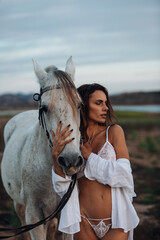 Portrait of a white horse and sexy woman. Beautiful glamour woman with a horse. Portrait of a beauty undressed woman with horse.