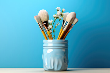 Artistic brushes and a delicate white flower in a jar on a blue wall background