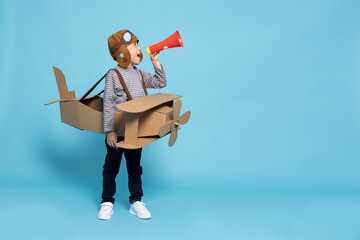 Asian little boy aviator holding megaphone and playing with cardboard airplane isolated on blue sky...