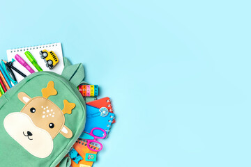 Back to school, education concept Deer green backpack with school supplies - notebook, pens, eraser rainbow, numbers isolated on blue background Top view Copy space Flat lay composition