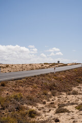 Desert landscape of white sand and desert shrubs. Asphalt road, mountains in the background. Sky with big white clouds. Lanzarote, Canary Islands, Spain.