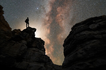 Silhouette of a hiker standing on the rock, on the milky way galaxy background.