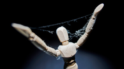 A wooden mannequin with raised arms is covered with cobwebs.