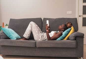 woman lying relaxed in casual wear lying on sofa and reading book at home