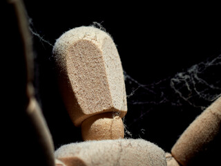 A wooden mannequin with raised arms is covered with cobwebs.