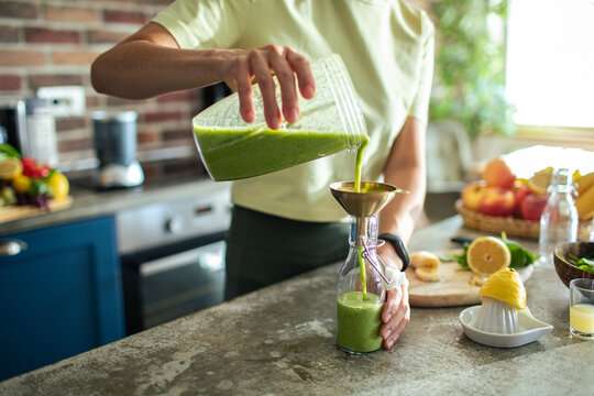 Close up of a woman pouring a healthy smoothie in a glass bottle