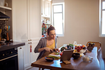 Young woman preparing a organic meal with the help of her tablet in the kitchen