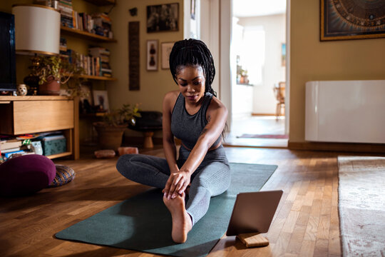 Young woman stretching and looking at the tablet in the living room
