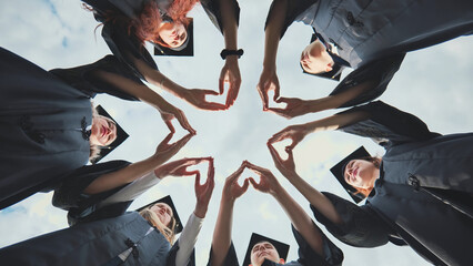 A group of college graduates stand in a circle and make hearts out of their palms.