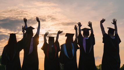 Silhouettes of graduates in black robes wave their arms against the evening sunset and toss their caps. - obrazy, fototapety, plakaty