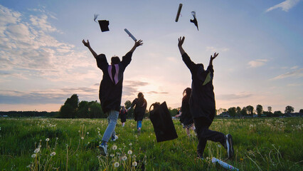 College graduates run to meet the sun and toss their caps and diplomas.
