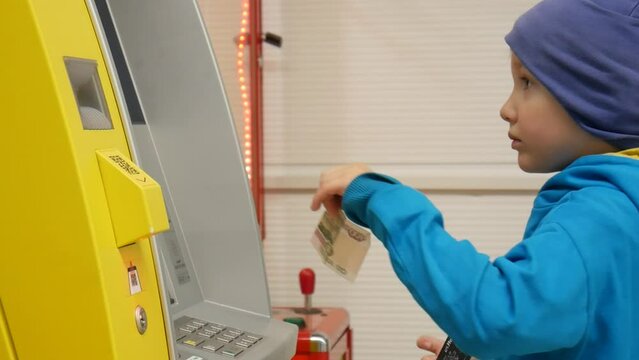 A cute boy inserts a bill into the ATM bill acceptor