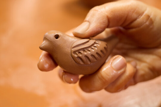 Unrecognizable potter master holding bird sculpture from clay clay in hand.