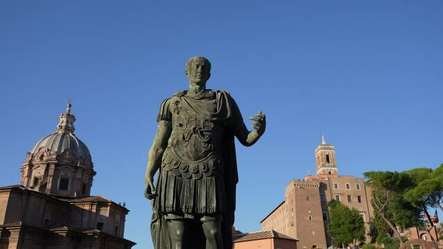 Tilt down portrait of Julius Caesar statue with church of Saint Luca e Martina on background - bronze copy of statue in Capitol on sunny day with blue sky. Shooting in slow motion.