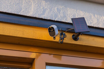 Close up view of high-tech outdoor security camera equipped with solar panel mounted on villa's facade. Sweden. - obrazy, fototapety, plakaty