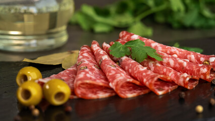 Fresh slices smoked sausage with spices and seasonings on stone cutting board with olives and parsley. Cold cuts. Meat. Food